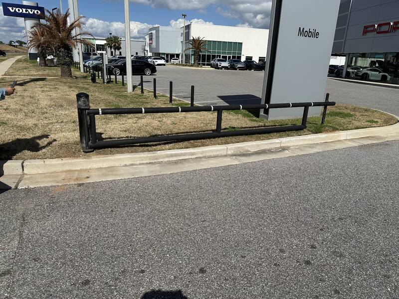 Finished black steel pipe barrier with white bands running along a curb at the edge of a paved parking lot
