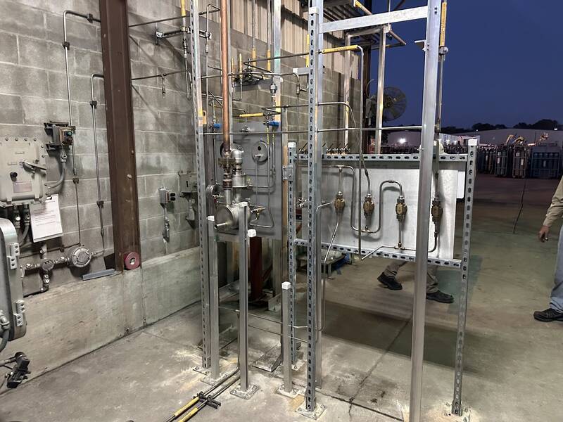 Galvanized steel strut frames holding stainless tubing, valves and gauges against a block wall at an industrial facility at dusk